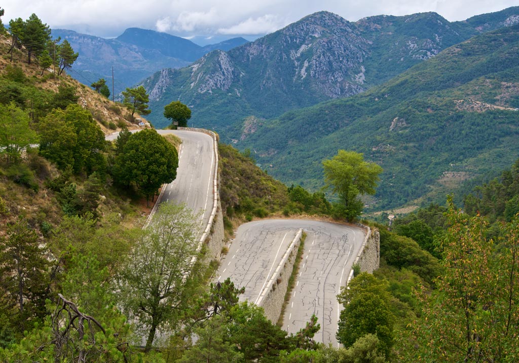 A mountain road snakes its way down the hillside amidst green trees and long views