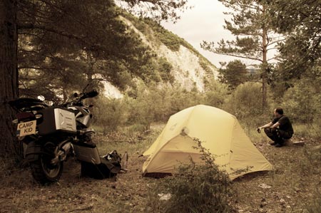 Guy squats by tent and bike, enjoys beer in free campsite
