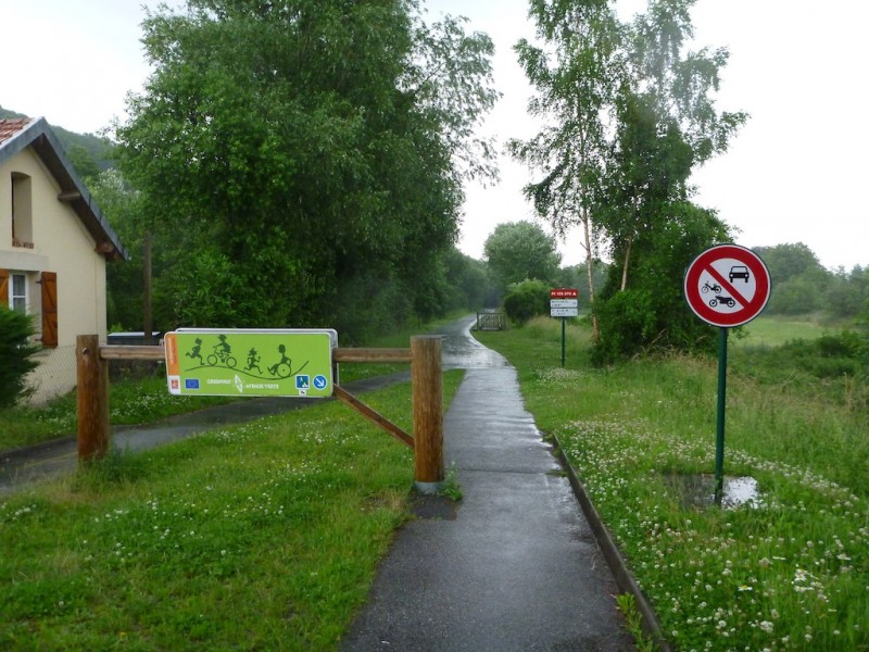 A wet cycle path disappears into the distance past a barrier prohibiting larger traffic