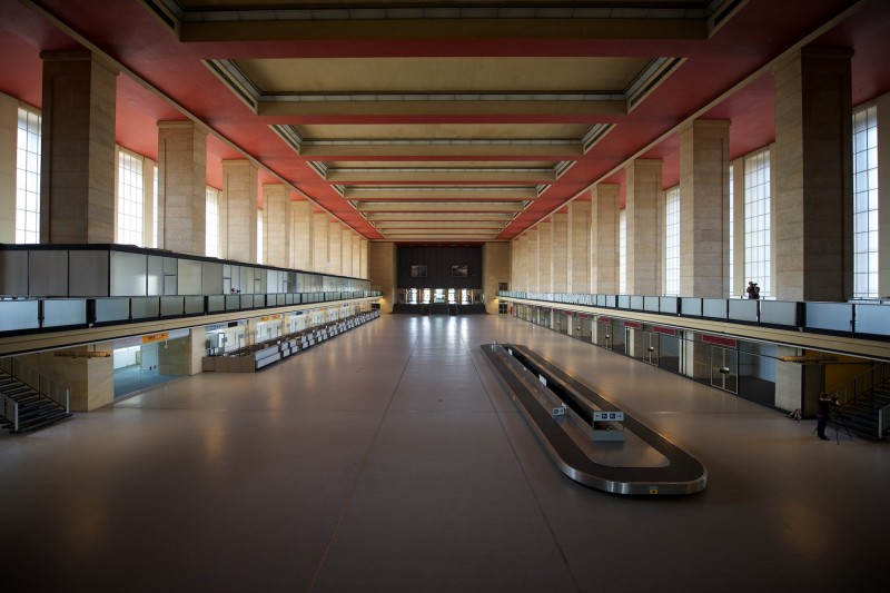 An empty arrivals / baggage reclaim hall in a vaguely art deco derelict airport