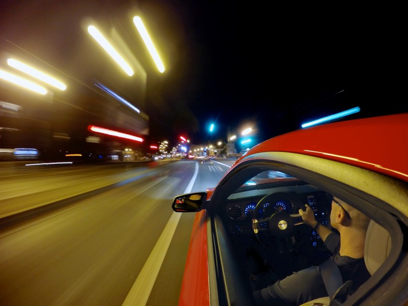 Semi-long exposure with camera clamped to the side of a red car as it drives down a darkened city road