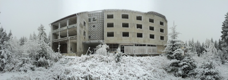 Panoramic view of the exterior of a derelict hotel, broken windows looking out over frozen grounds in the middle of winter
